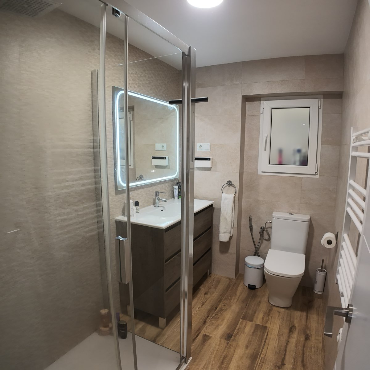 Baño reformado en Tarragona con ducha de obra, mampara de cristal y suelo porcelánico imitación madera