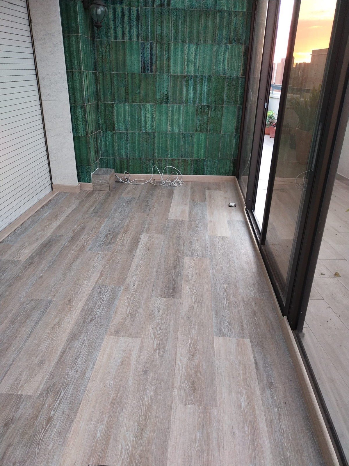 Terraza reformada en Tarragona con suelo laminado y pared de azulejo verde decorativo