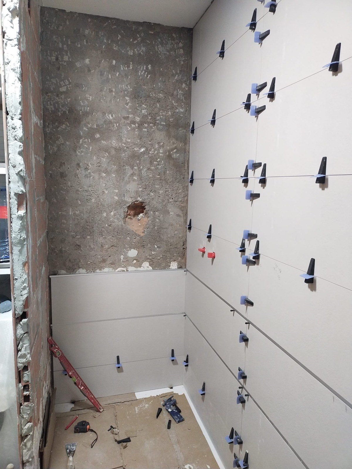 Reforma de baño con alicatado blanco en proceso y crucetas niveladoras de azulejo