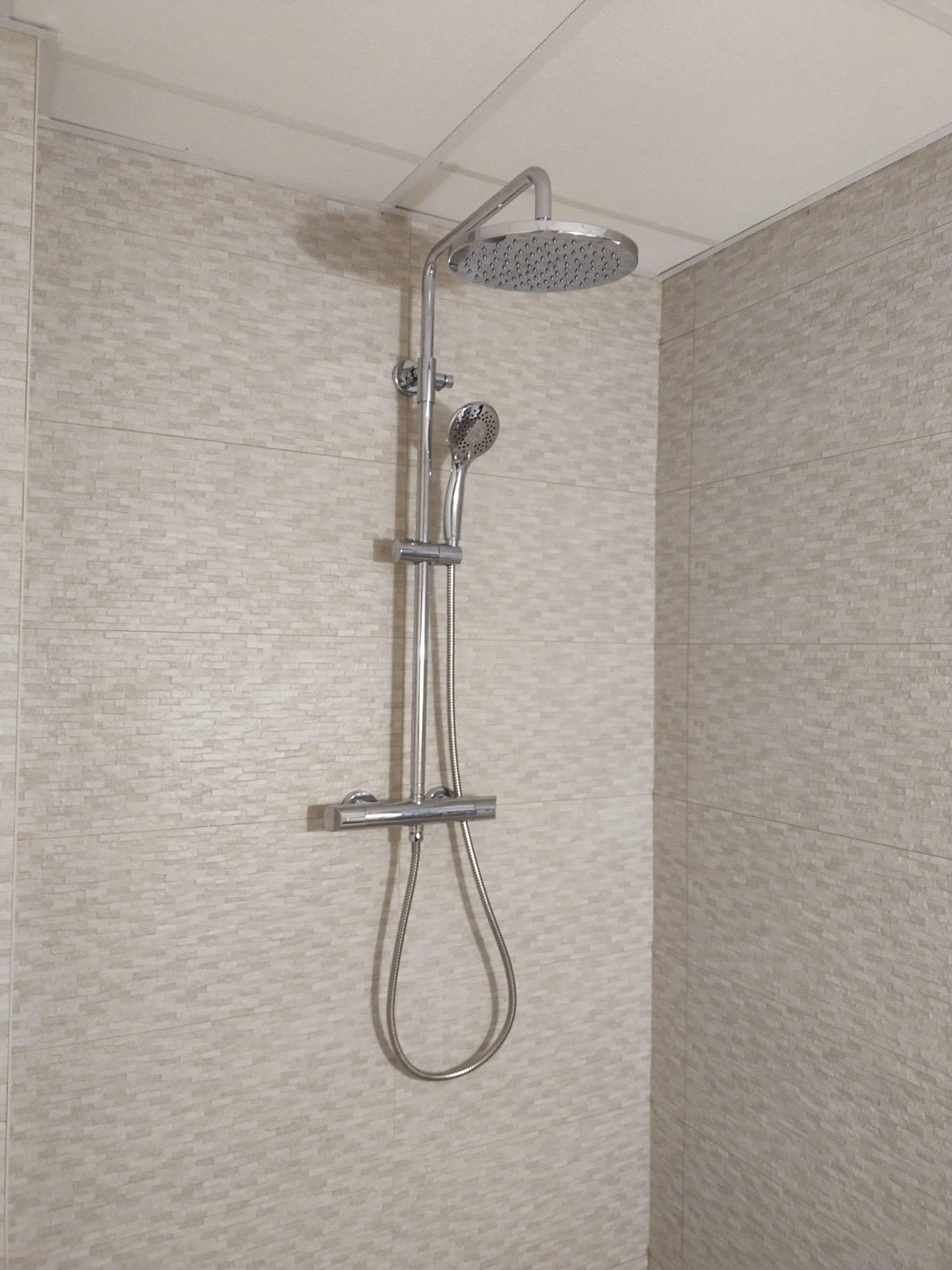 Columna de ducha con rociador cromado sobre alicatado beige texturizado en baño reformado