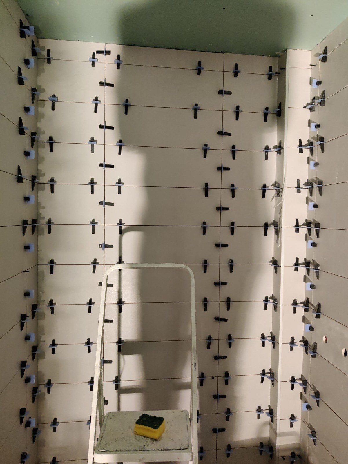 Alicatado de paredes de baño en obra con crucetas niveladoras y techo verde