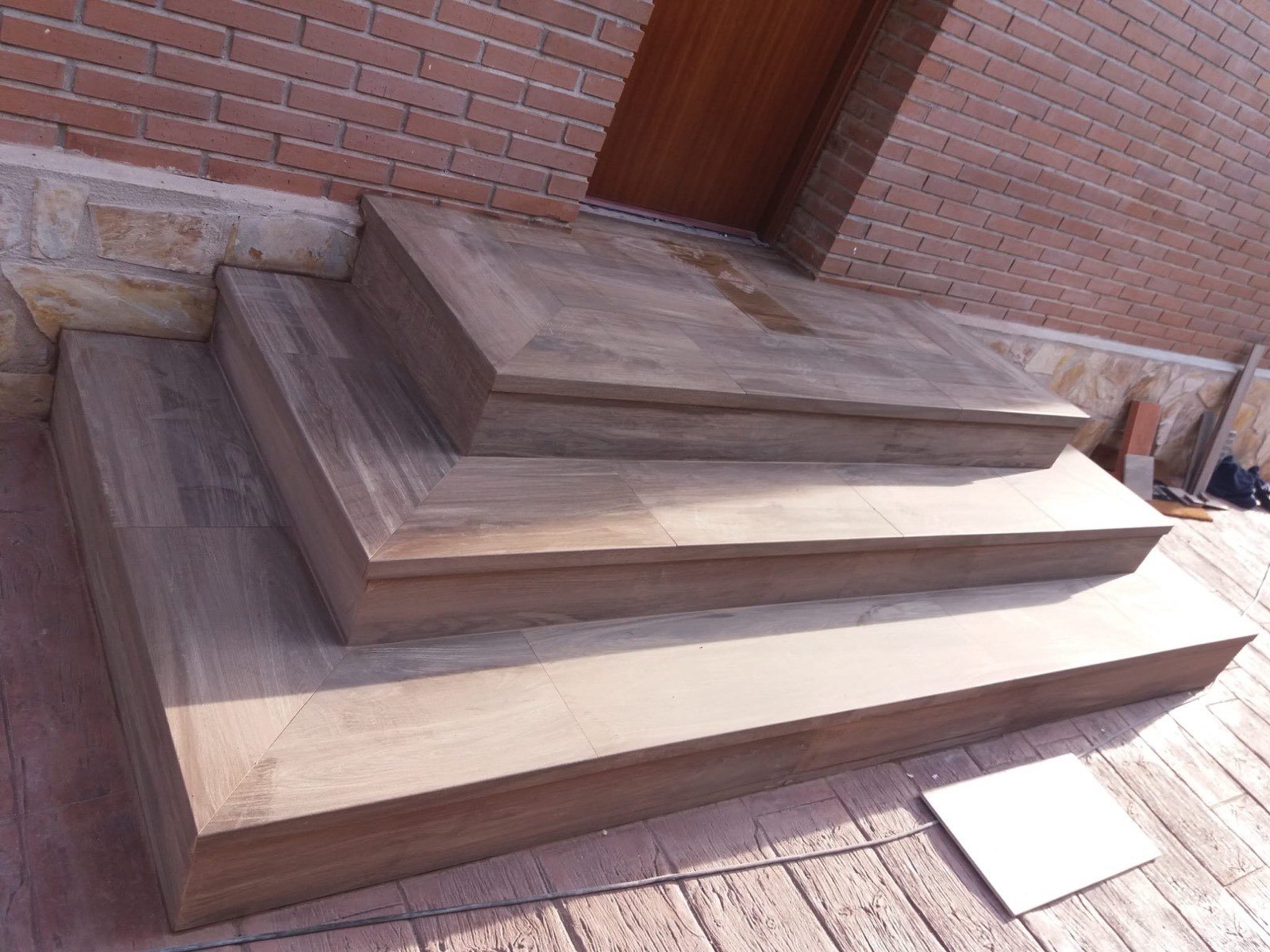 Escalones exteriores revestidos con porcelánico imitación madera junto a fachada de ladrillo