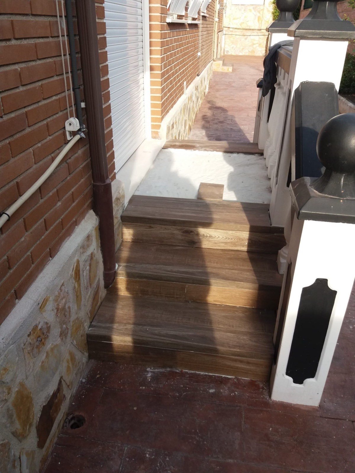 Escalones de entrada reformados con porcelánico tipo madera y barandilla blanca
