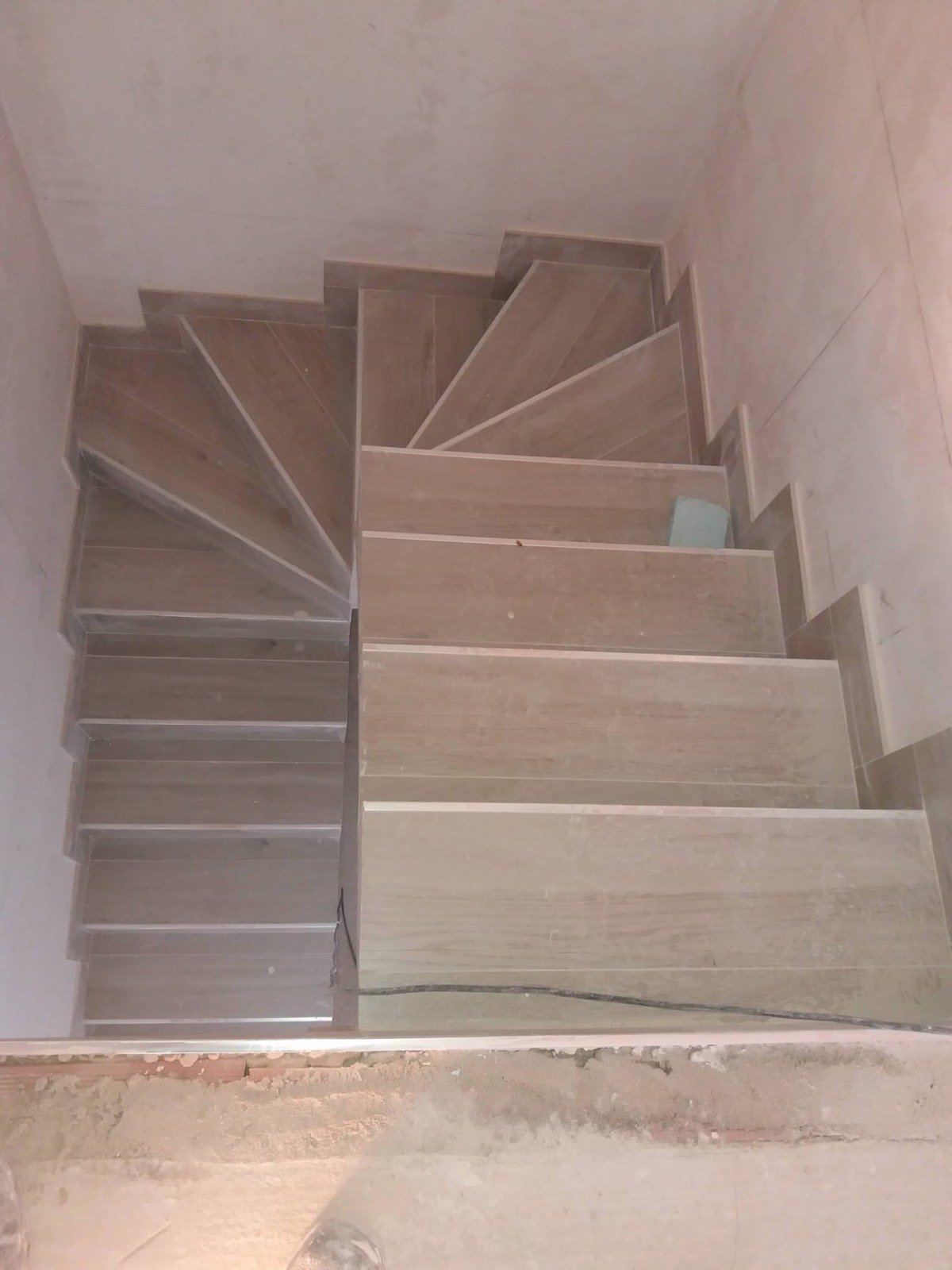 Escalera interior de caracol revestida con peldaños porcelánicos imitación madera